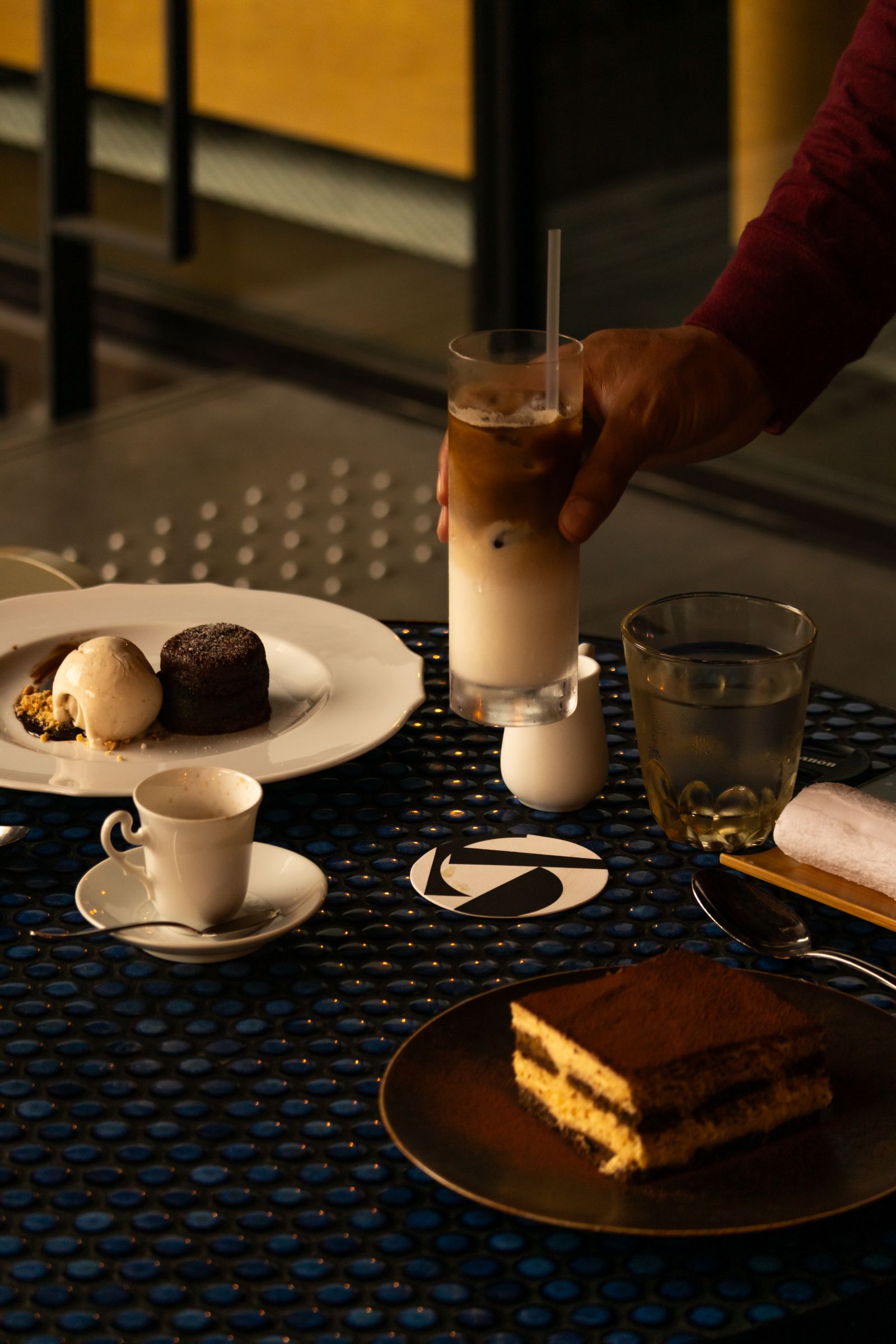 Tiramisu on a table as a hand lifts an iced coffee